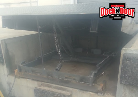 Open mechanical dock leveler pit showing the underside spring mechanism