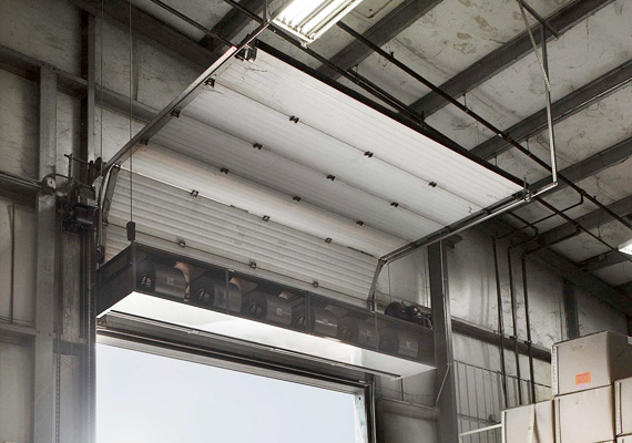 Overhead sectional door panel raised with an air curtain unit mounted above it