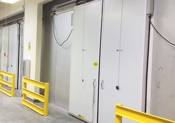 Vertical bi-parting cooler doors in a cold storage facility corridor