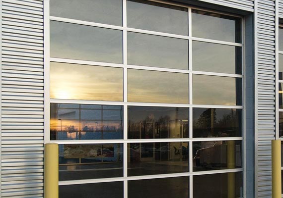 Full-view glass sectional door on a metal building exterior, reflecting a sunset sky