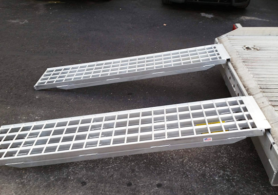 Pair of aluminum walk ramps extended from a trailer bed to the ground