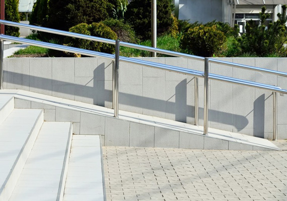 Concrete pedestrian ramp with a stainless steel handrail next to a stairway