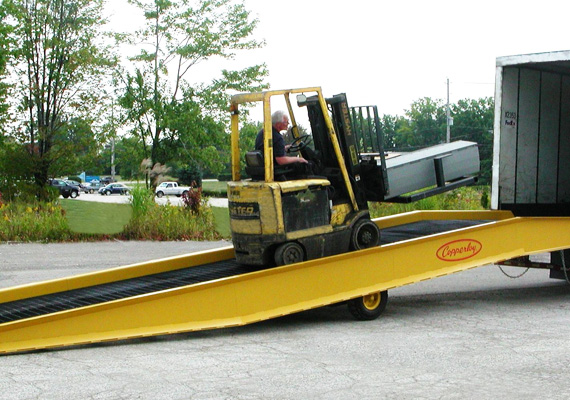 Forklift driving up a portable yard ramp into a trailer